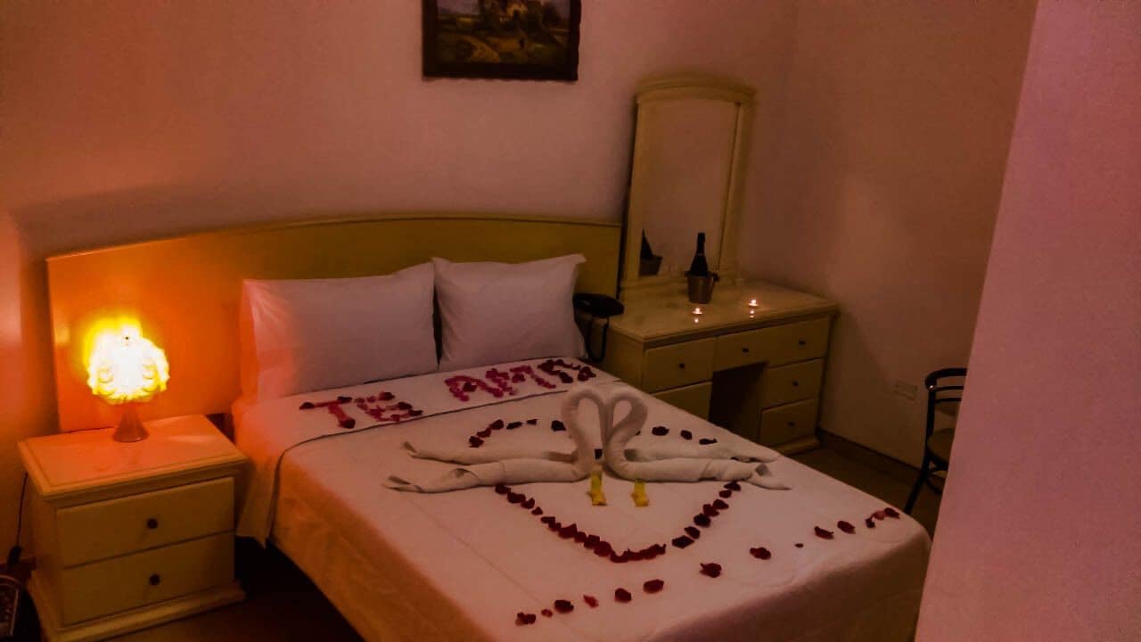 Una habitación de hotel con una cama, una mesita de noche con lámpara, un aparador y un espejo.