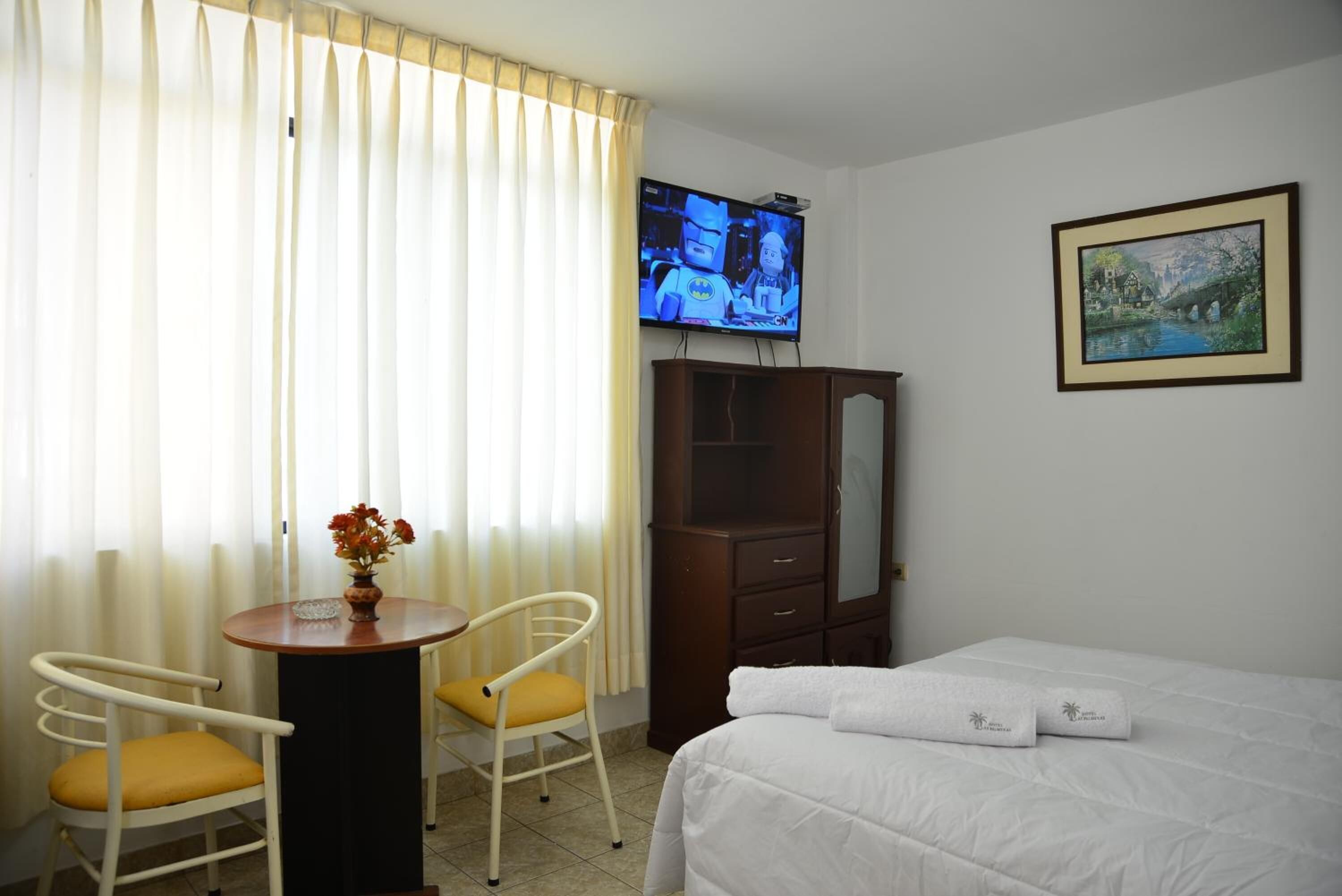 A hotel room with a bed, a TV, a wooden cabinet, a desk with a chair, and a painting on the wall.