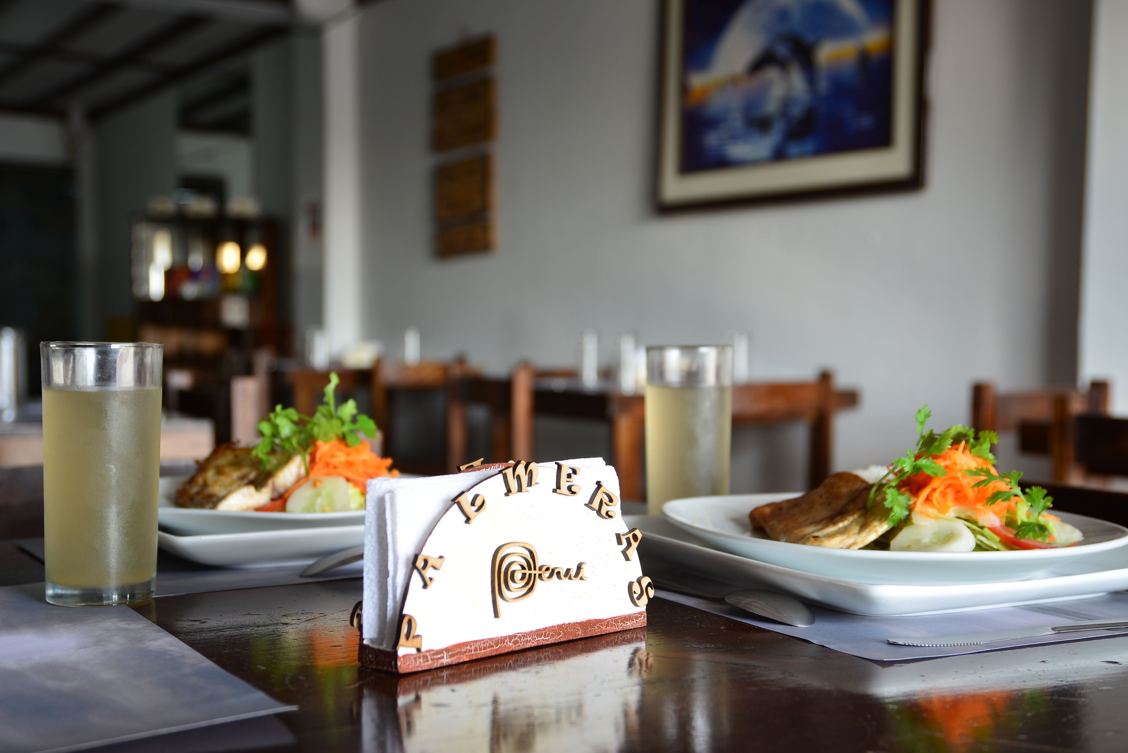 A restaurant setting with a table set for two, featuring plates of food and glasses of a light-colored beverage.