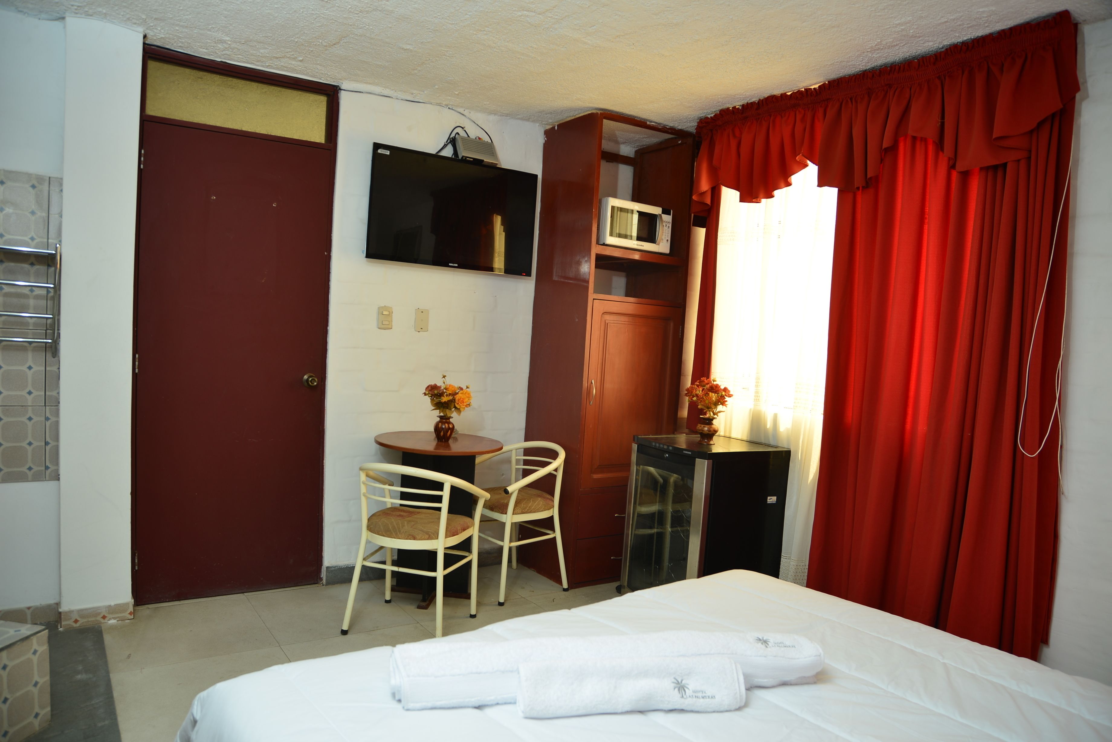 A hotel room with a bed, a desk with a chair, a microwave, and a TV on the wall.