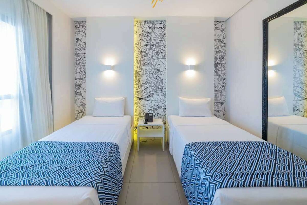 A hotel room with two single beds, a small table with a phone, and a wall with a mural.