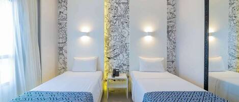 A hotel room with two single beds, a small table with a phone, and a wall with a mural.
