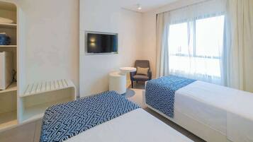 Habitació d'hotel amb dos llits, una televisió, una cadira i una finestra amb cortines.