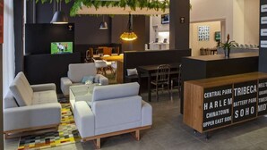 Eine moderne Lobby mit Sitzbereichen, einem Empfangstresen und einem Fernsehbildschirm.