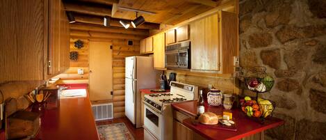 Eine Holzhütte mit einer Küche, einem roten Arbeitsplatz, einem Herd, einem Kühlschrank und einer Steinwand.