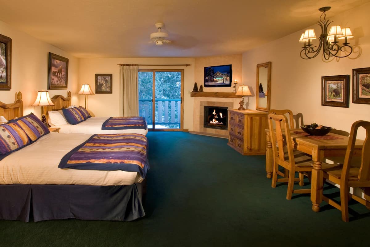 A hotel room with two beds, a fireplace, a dining table with chairs, and a television on the wall.
