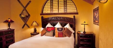 A neatly made bed with multiple pillows and a headboard, flanked by two nightstands with lamps and a small statue.