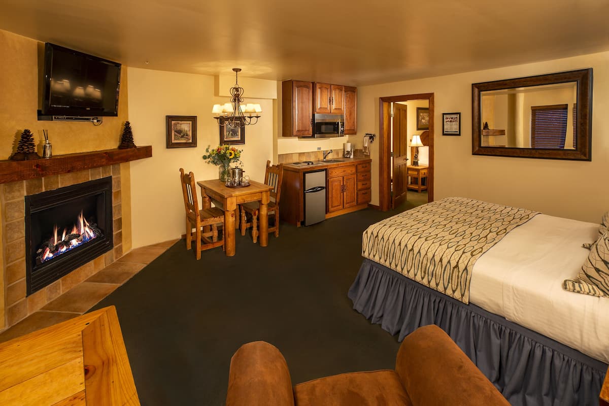 A hotel room with a fireplace, a dining area, a kitchenette, and a large bed.