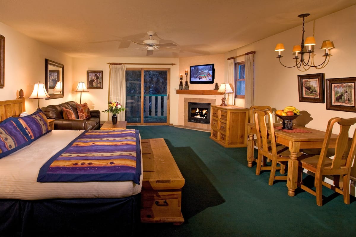 A cozy room with a bed, a fireplace, a dining table with chairs, a television, and a balcony with a view.