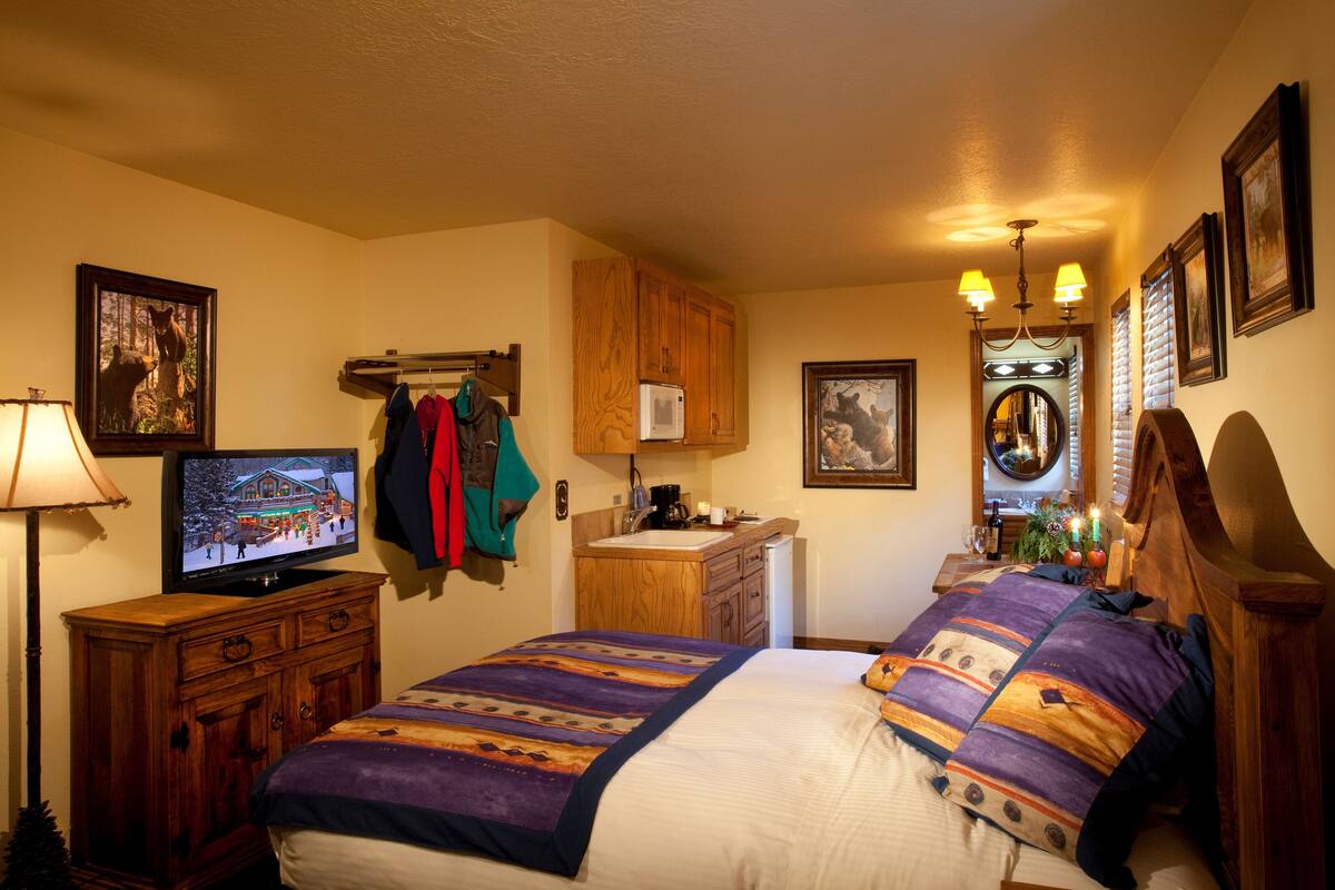 A bedroom with a bed, wooden dresser, television, and a small bathroom area.