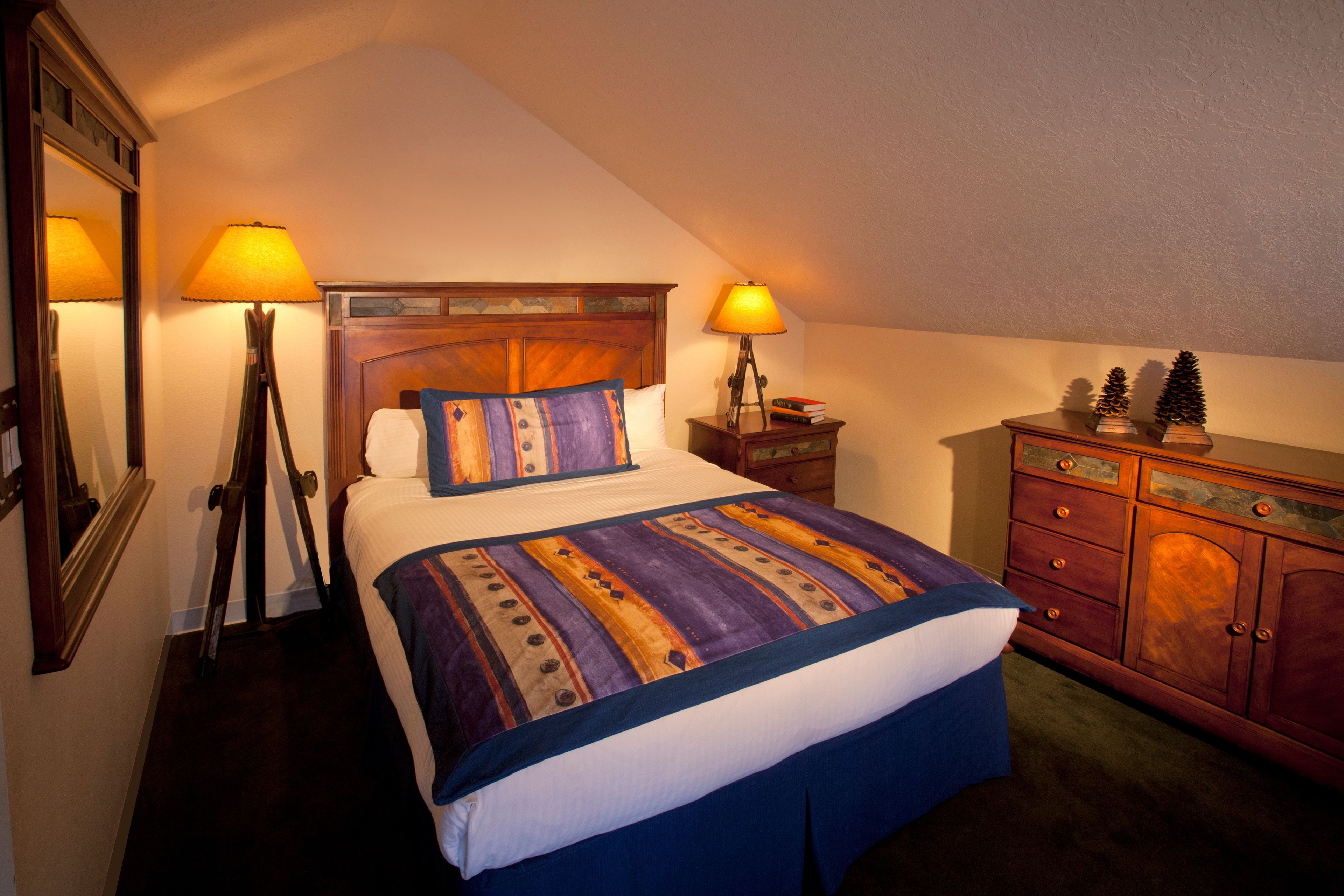 A neatly arranged bedroom with a bed, two bedside lamps, a dresser, and a mirror.