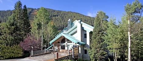 A building with a blue roof and white walls, surrounded by trees and a mountain in the background.