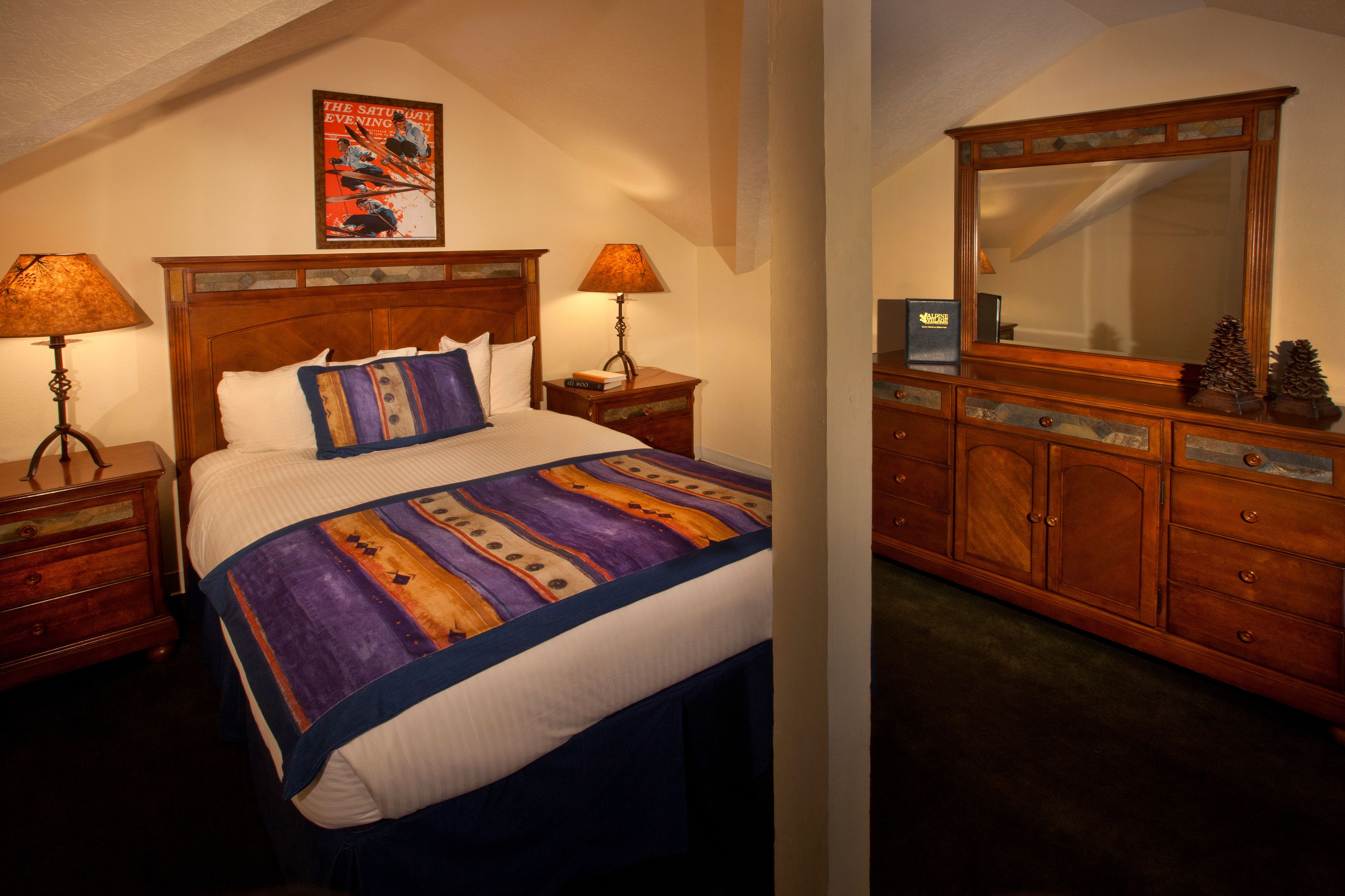 Une chambre à coucher avec un grand lit, deux tables de chevet avec des lampes, une commode en bois et une affiche accrochée au mur.