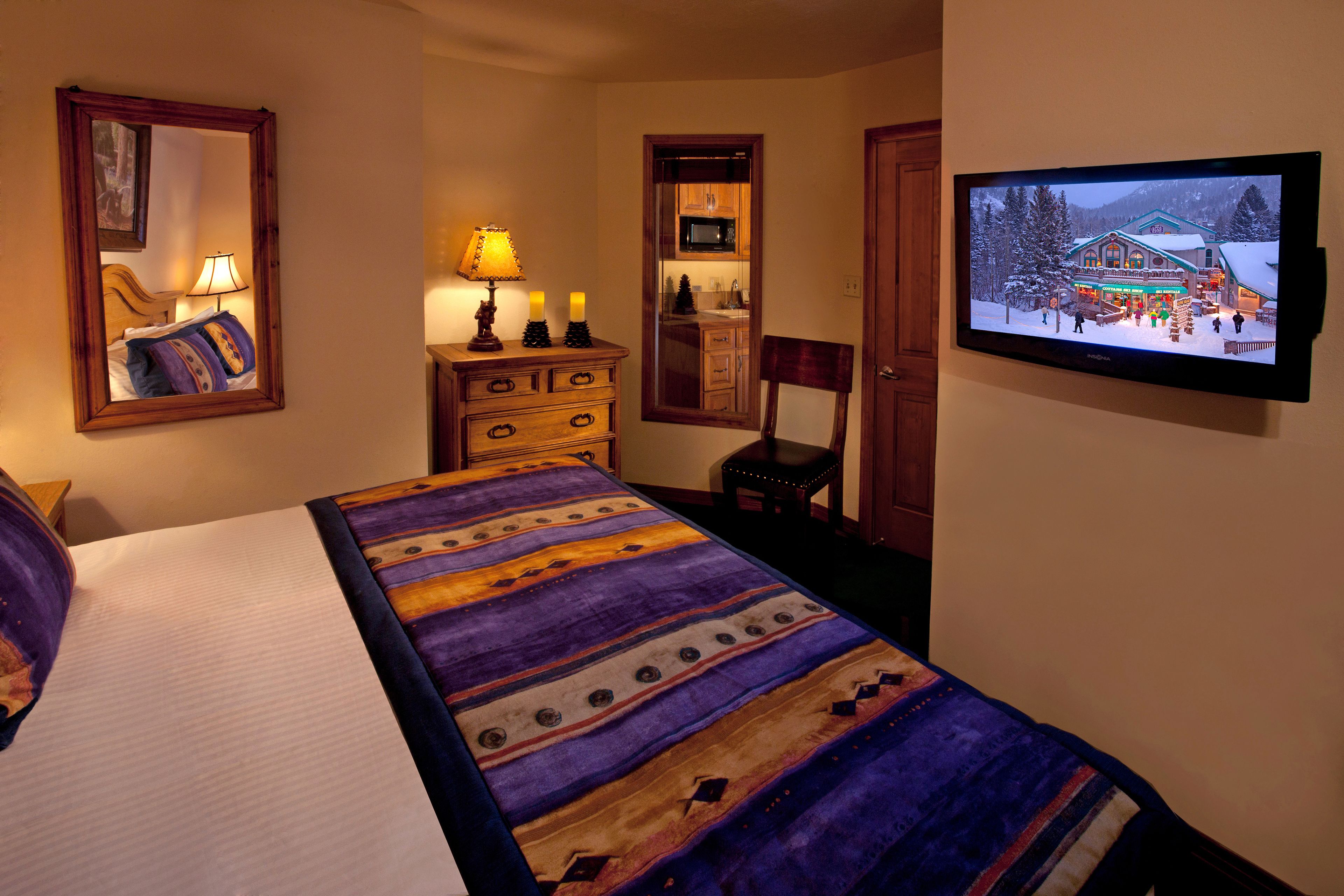 Une chambre d’hôtel avec un lit, une commode, une télévision et un miroir.