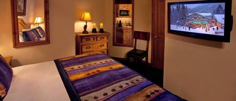 Une chambre d’hôtel avec un lit, une commode, une télévision et un miroir.