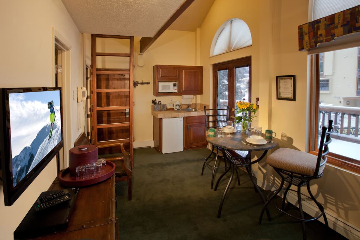 A cozy living room with a television, a coffee table, and a dining area with chairs and a table.