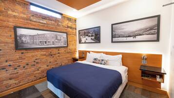 Une chambre d’hôtel moderne avec un mur en briques, un grand lit recouvert d’une courtepointe bleue et trois photographies encadrées accrochées au mur.