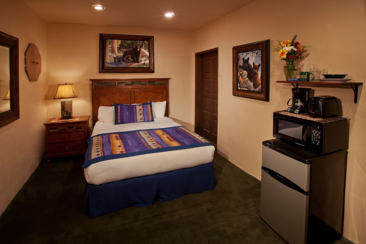 A hotel room with a bed, a nightstand, a lamp, a microwave, and a refrigerator.