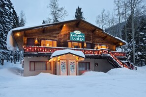 En træhytte med skiltet "Cottam's Lodge", med en balkon med gelændere og en trappe op til indgangen.