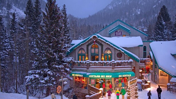 Uma loja de aluguel de esquis com uma placa indicando "COTTAMS SKI SHOP" e "ALPINE VILLAGE SUITES".