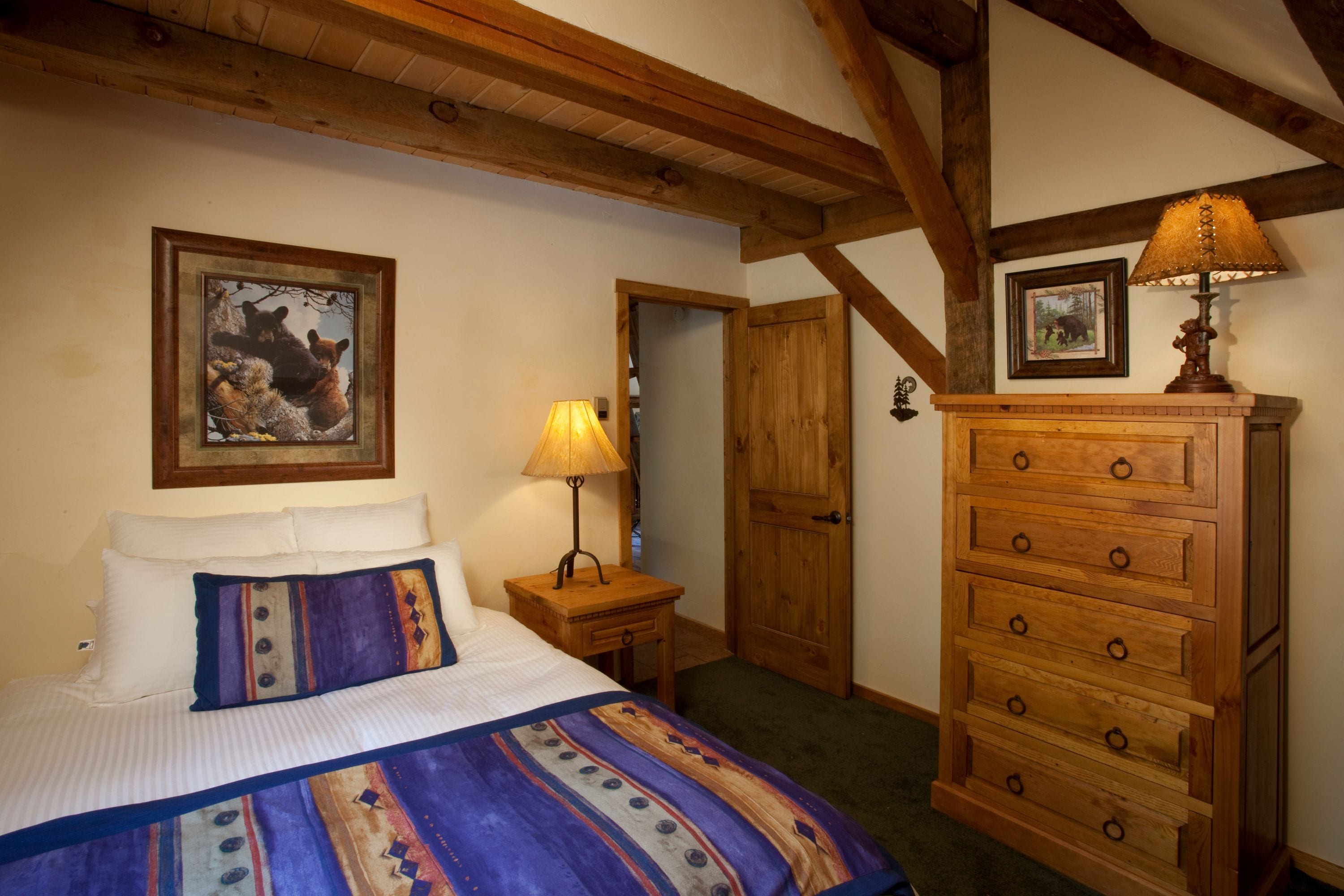 A bedroom with a bed, wooden dresser, and a lamp.