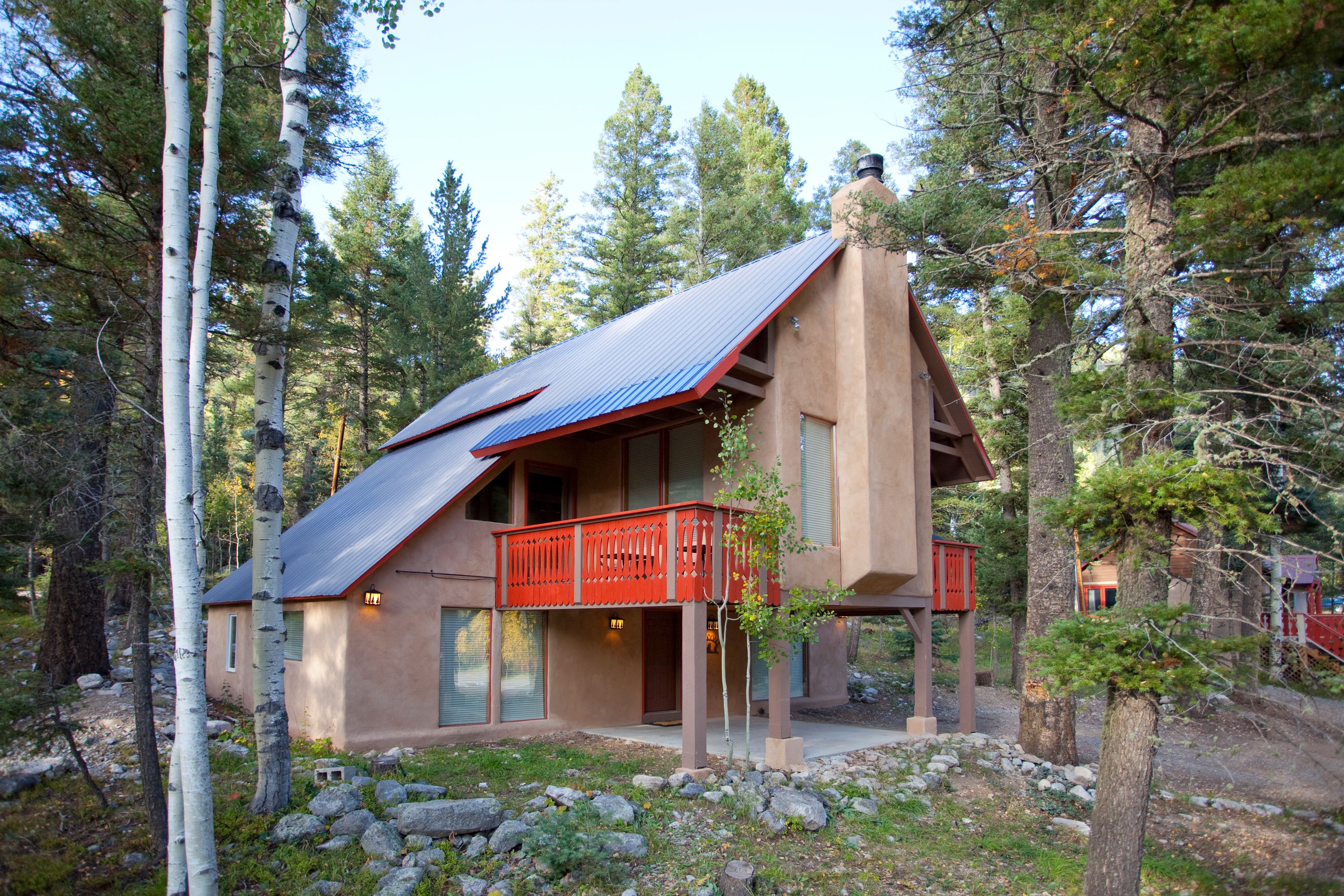 Une cabane à deux étages avec un balcon rouge, entourée d’arbres et de rochers.