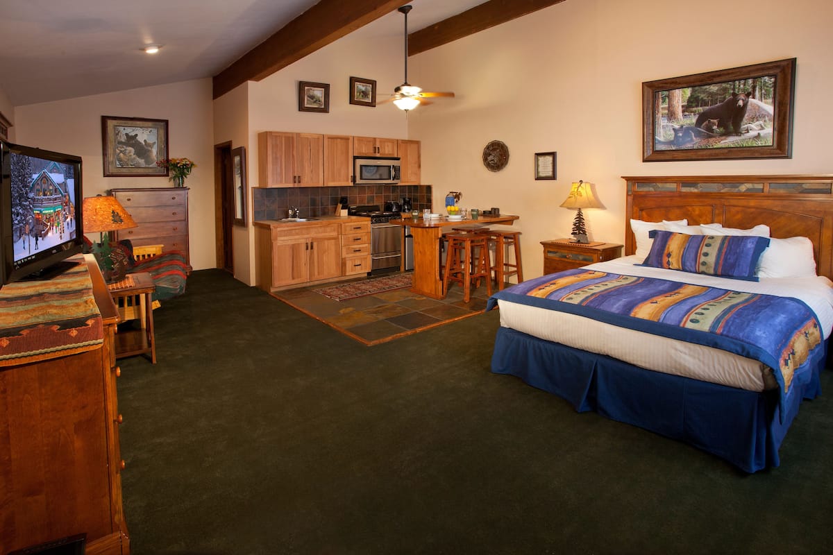 A bedroom with a large bed, a desk, and a kitchenette.