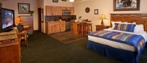 A bedroom with a large bed, a desk, and a kitchenette.