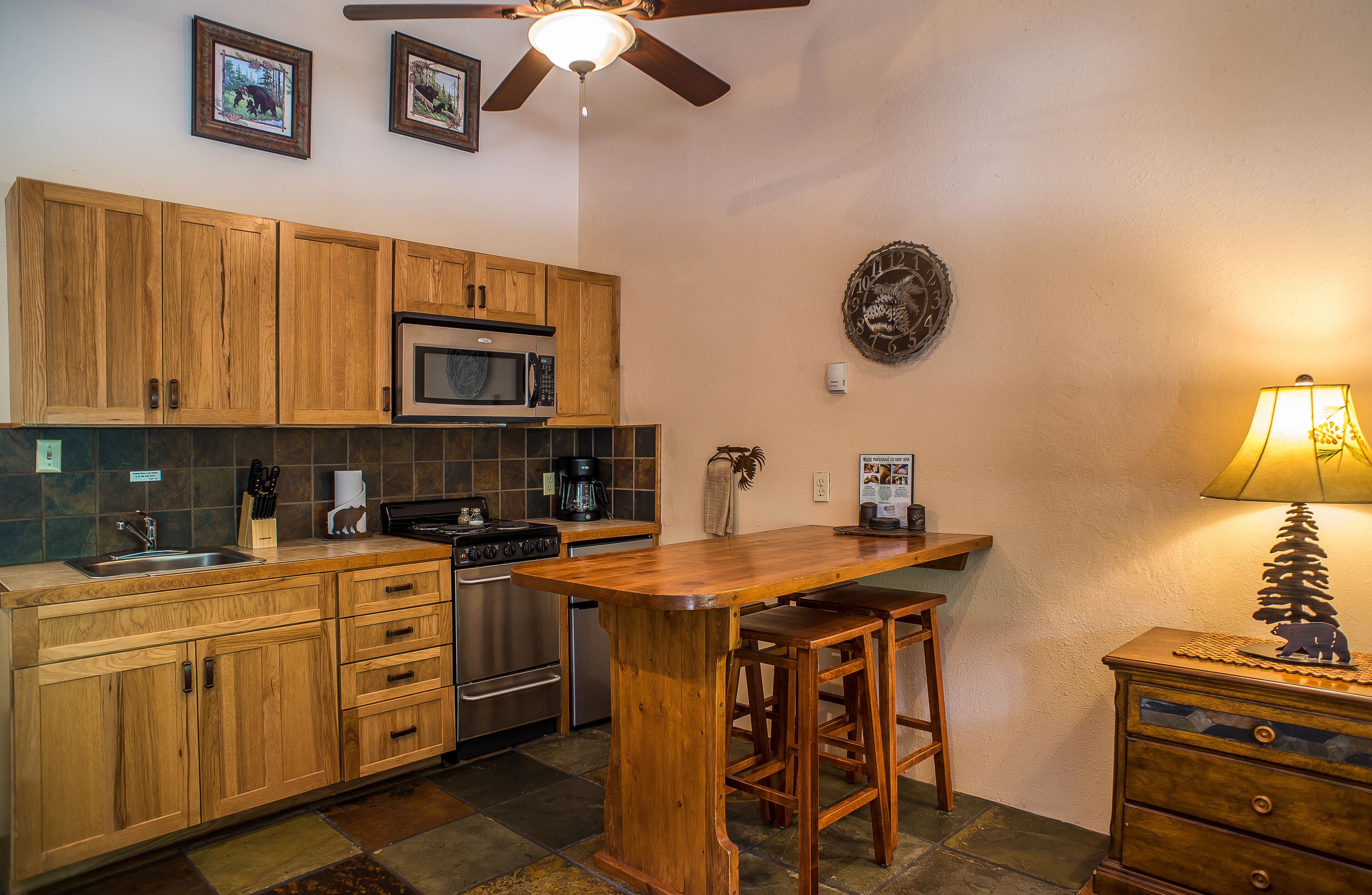 A kitchen with wooden cabinets, a microwave, a stove, and a bar area with stools.