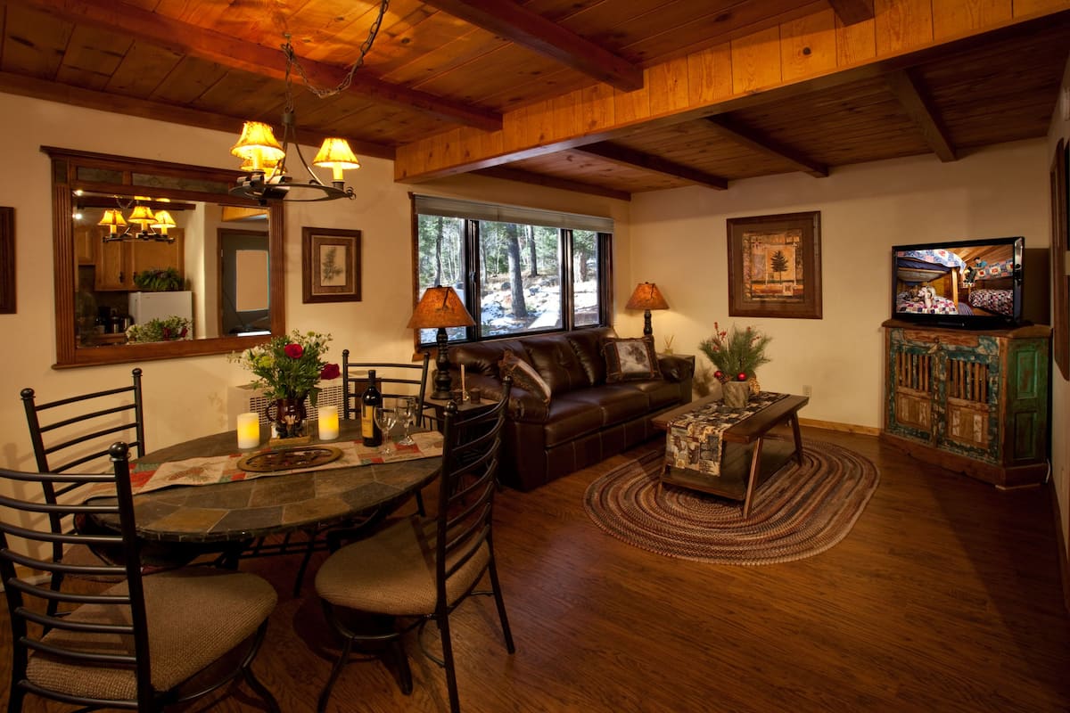 A cozy living room with a wooden ceiling, a stone-tiled dining table, leather sofa, and a television on a cabinet.