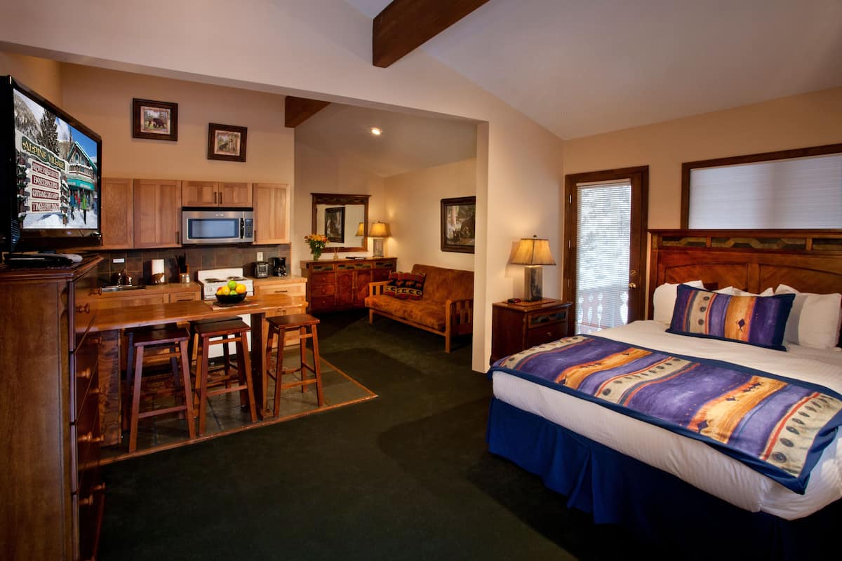 A hotel room with a bed, a desk with a chair, a microwave, a television, and a small kitchen area.