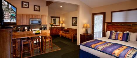 A hotel room with a bed, a desk with a chair, a microwave, a television, and a small kitchen area.