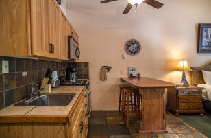 A kitchen with wooden cabinets, a sink, a stove, and a bar area with stools.