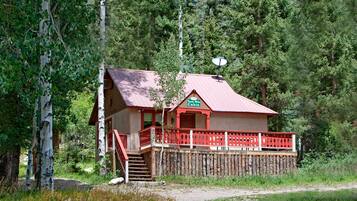 A cabin with a red roof and a balcony, surrounded by trees and a wooden fence.