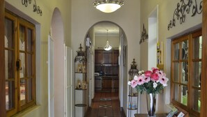 Un couloir avec un sol carrelé, une porte en bois, une étagère en métal avec des bocaux et un vase rempli de fleurs.