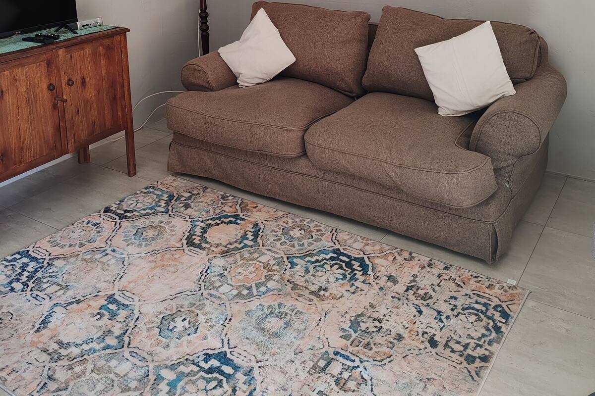 Ein Wohnzimmer mit einer braunen Couch, zwei gerahmten Bildern, einer Chandelierleuchtre, einer Lampe und einem Fernseher auf einer Holzkommode.