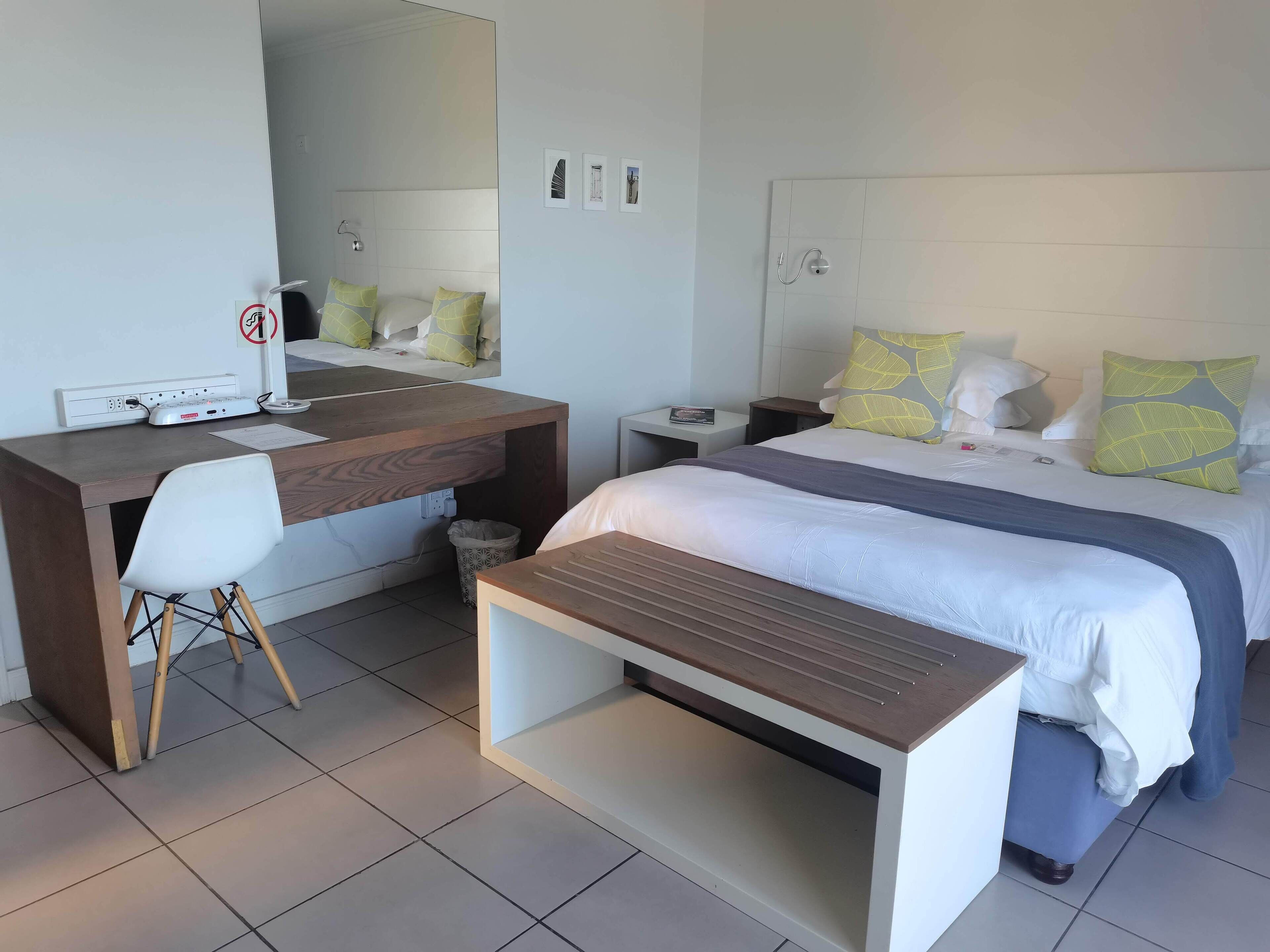 Een moderne hotelkamer met een bed, nachtkastje, bureau, stoel en een kleine prullenbak.