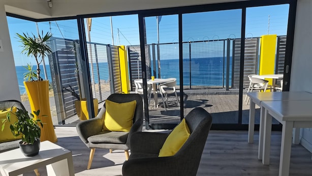Un interno moderno con ampie finestre, vista mare e un'area salotto con sedie e un tavolo.