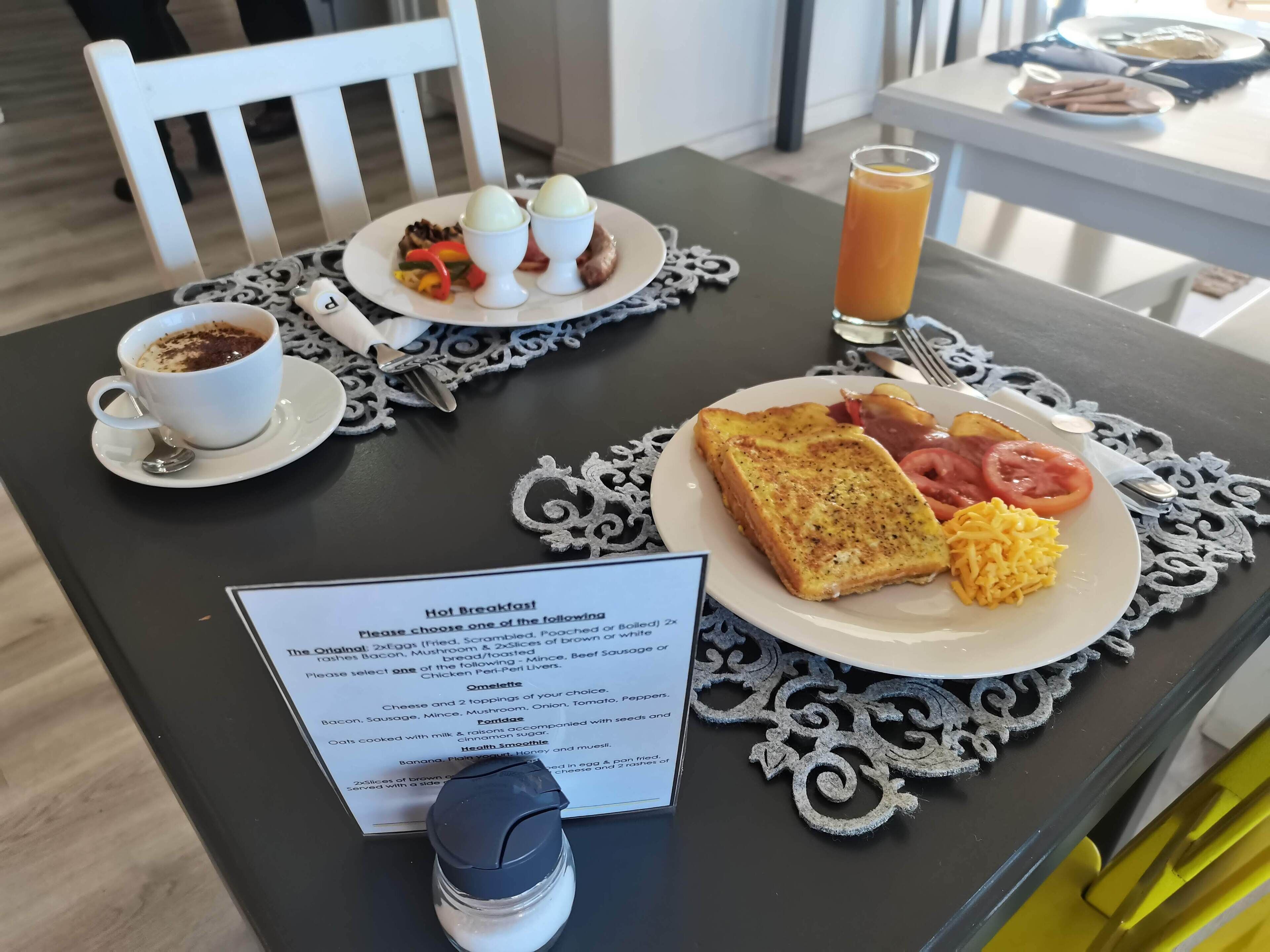 A breakfast table with a menu, a cup of coffee, scrambled eggs, toast, tomatoes, and a glass of orange juice.