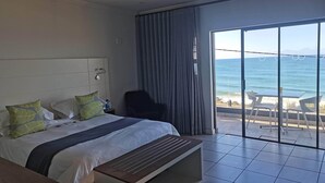Una camera d'hotel con un letto, una scrivania, una sedia e vista sull'oceano attraverso ampie finestre.
