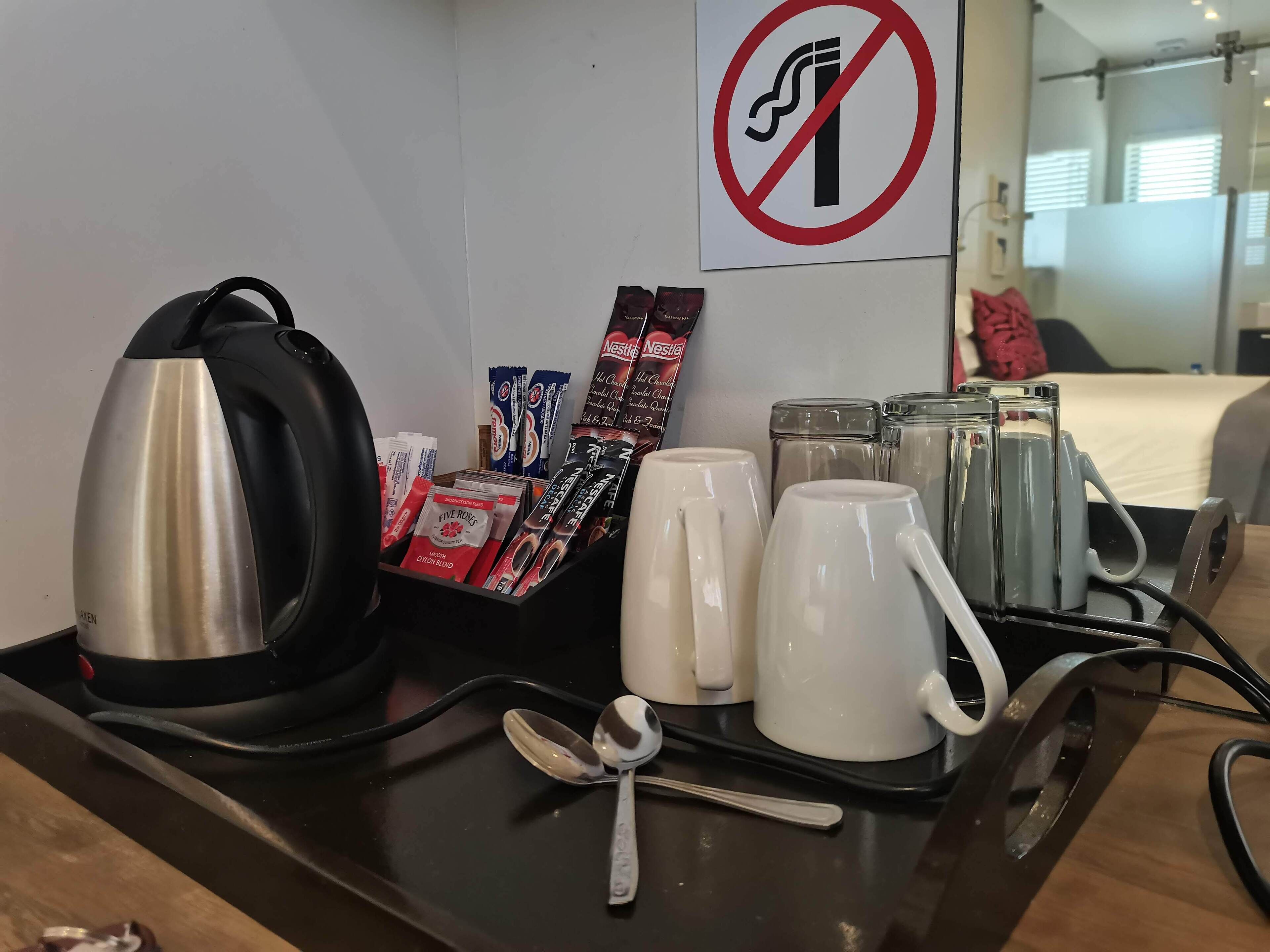 A hotel room's breakfast trolley with a kettle, coffee mugs, a spoon, and packaged food items.