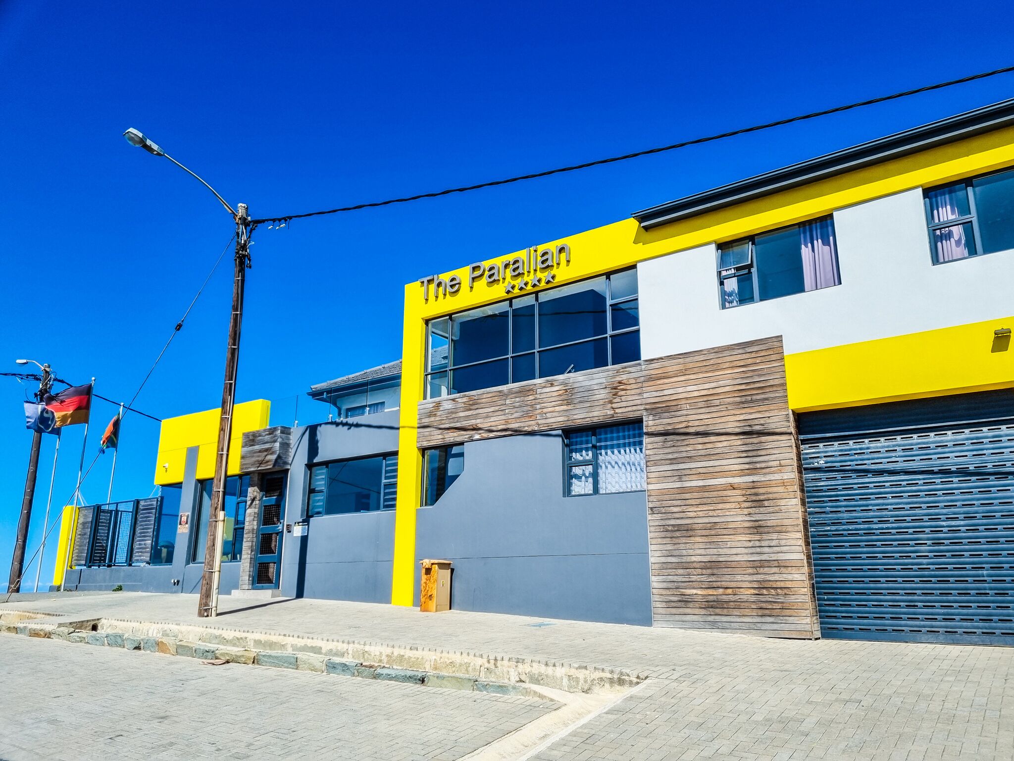 A modern building with a yellow and grey facade, a prominent sign reading "The Pallian," and a blue shuttered entrance.