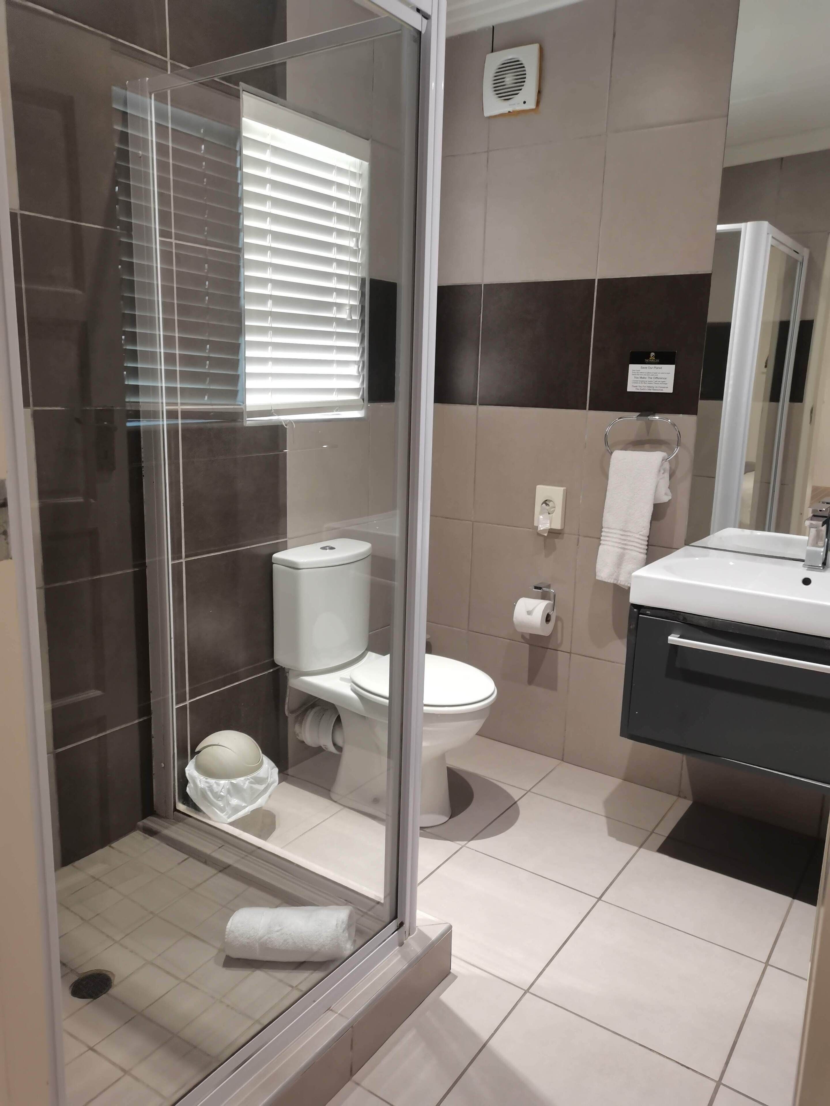 Un baño moderno con ducha de vidrio, inodoro y lavamanos con espejo.