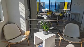 A modern, well-lit room with two white chairs, a small white table with a plant, and a view of the ocean through large windows.