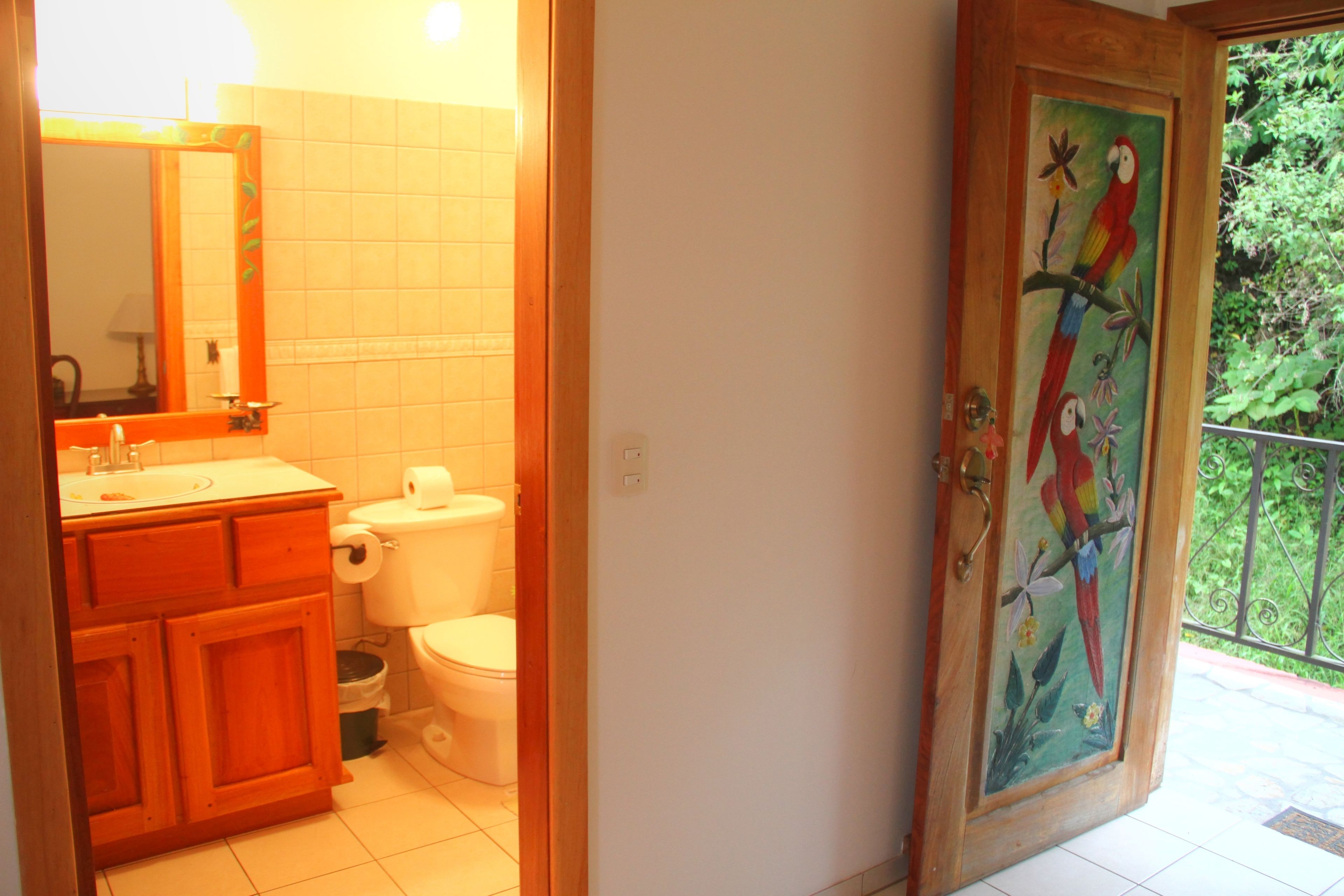 Un bagno con un mobile bagno in legno, un water e una porta decorata con un dipinto di un pappagallo colorato.