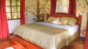 Quarto com cama grande, cortinas vermelhas e um mural de árvores e plantas na parede.