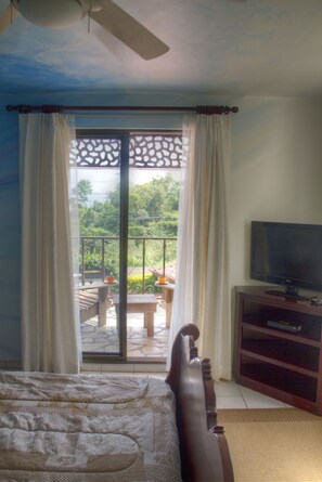 A bedroom with a bed, a television on a wooden stand, and a balcony with a table and chairs.