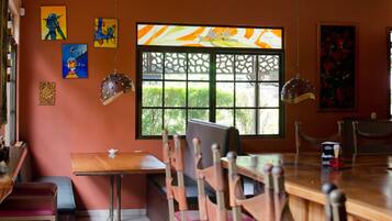 A restaurant interior with wooden tables and chairs, a large window with a decorative view, and various artworks on the walls.