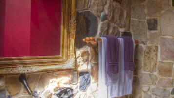 A bathroom with a stone wall, a red-framed mirror, a sink, and a toilet.