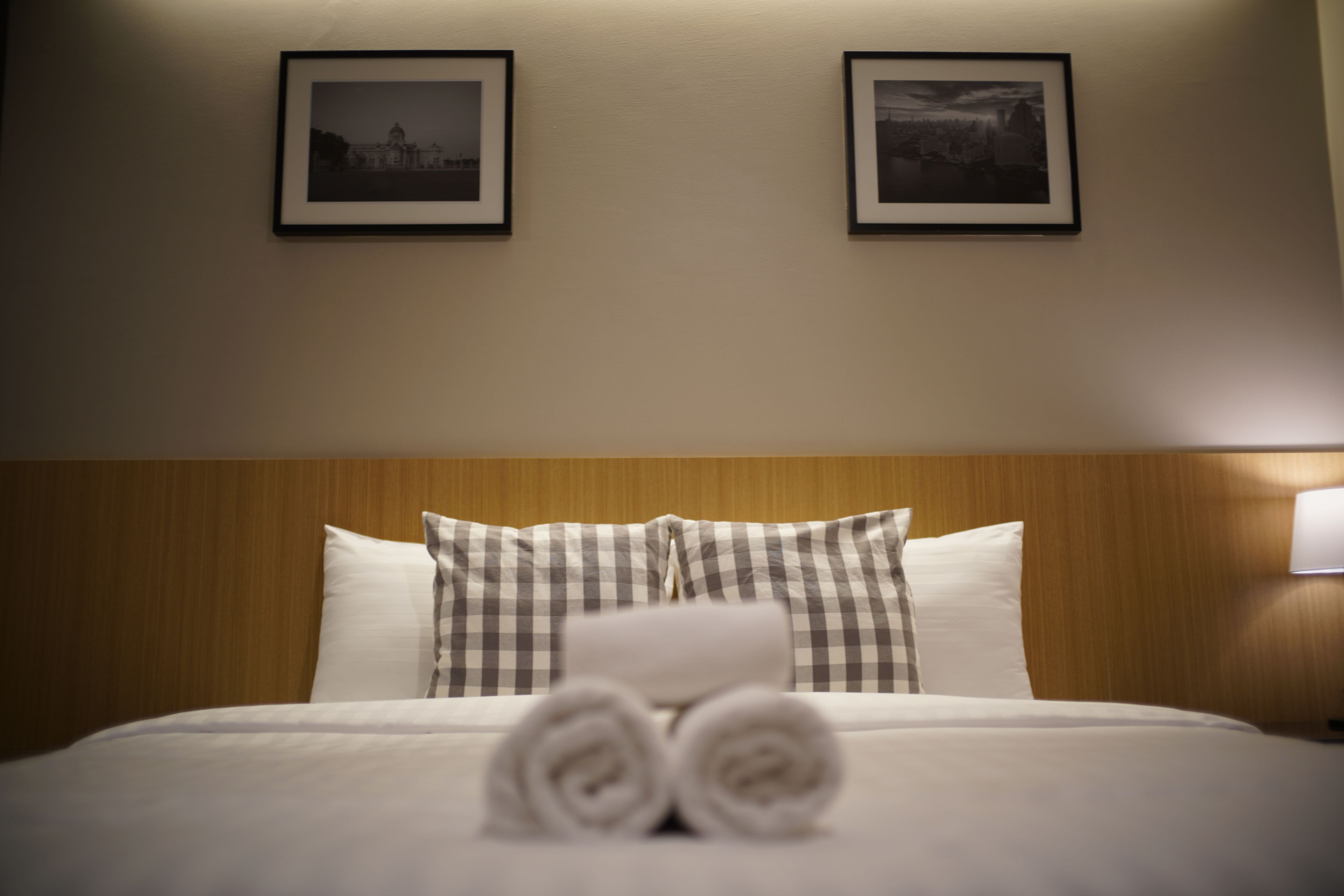 A neatly made bed with rolled towels, a wooden headboard, and two framed pictures on the wall.